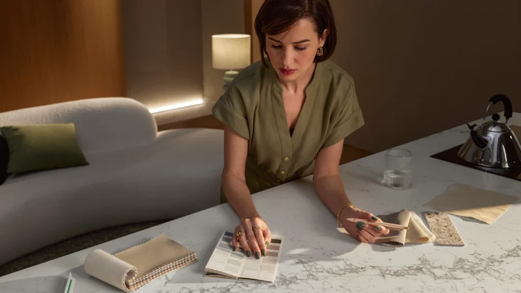 Woman reviewing material samples on a Caesarstone<sup>®</sup> Celestial Sky mineral surface benchtop in a softly lit living space