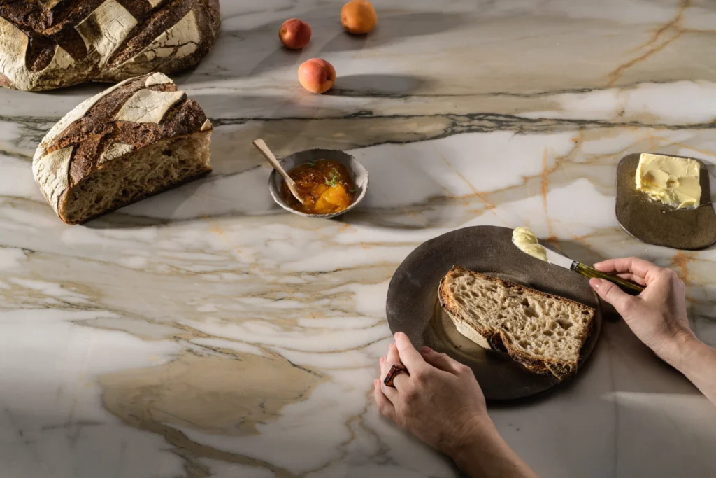 Caesarstone<sup>®</sup> Antikella warm veined marble-look benchtop styled with sourdough bread, honey and butter for everyday entertaining scene