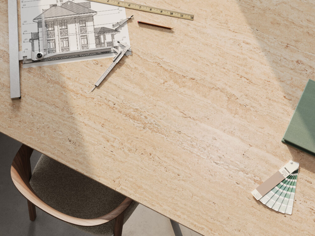 Close-up of Caesarstone<sup>®</sup> 551 Travina porcelain surface showcasing layered travertine-inspired textures styled with architectural drawings and design tools.