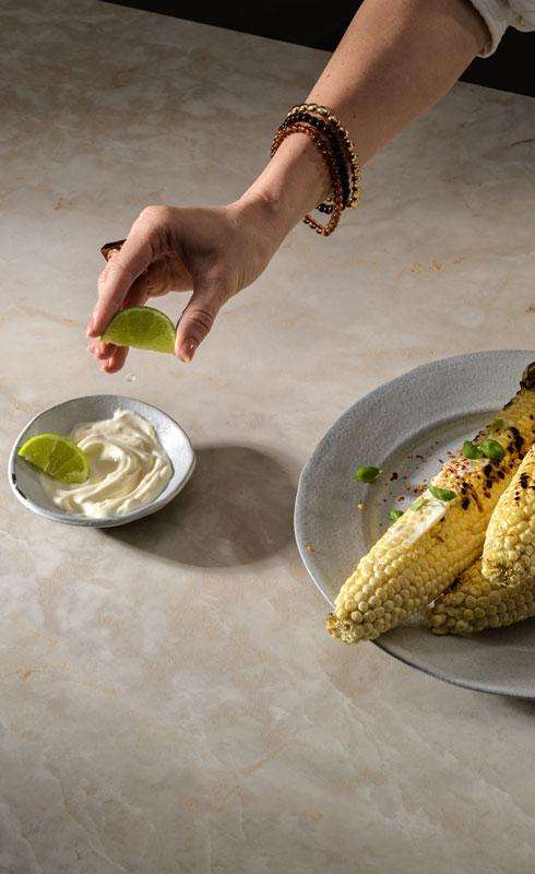 Caesarstone<sup>®</sup> Crestone™ 583 porcelain benchtop styled with grilled corn and lime in a contemporary kitchen setting