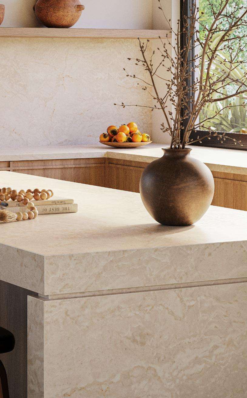 Caesarstone<sup>®</sup> Crestone™ 583 porcelain kitchen island benchtop with feathered veining in warm interior with garden outlook and ceramic vase styling