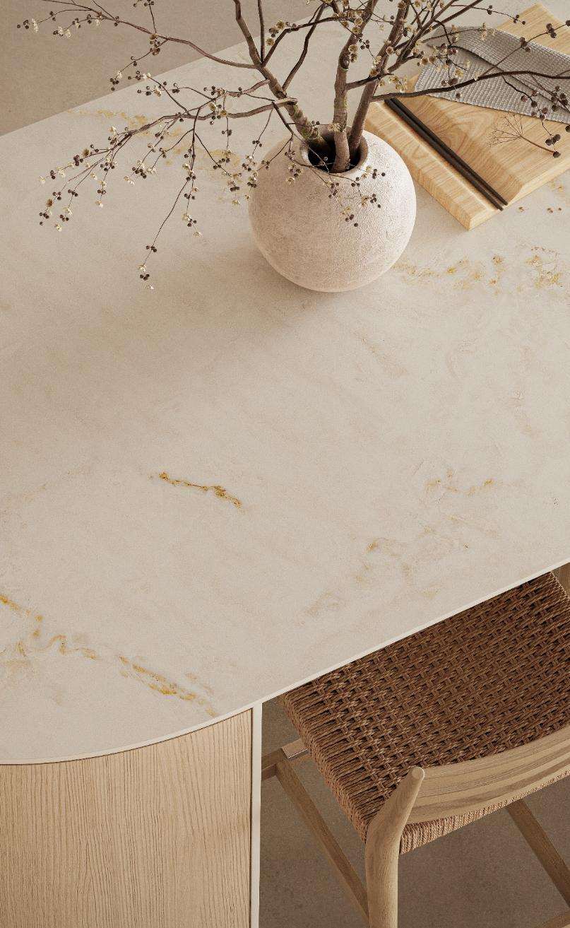 Caesarstone<sup>®</sup> Glacetta™ 537 porcelain round dining table surface with golden-brown veining, ceramic vase and rattan chair in warm interior