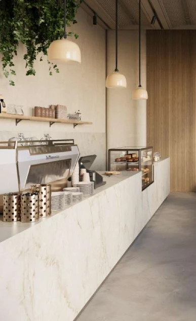 Caesarstone<sup>®</sup> Glacetta™ 537 porcelain benchtop in warm café or commercial interior with pendant lighting and timber shelving