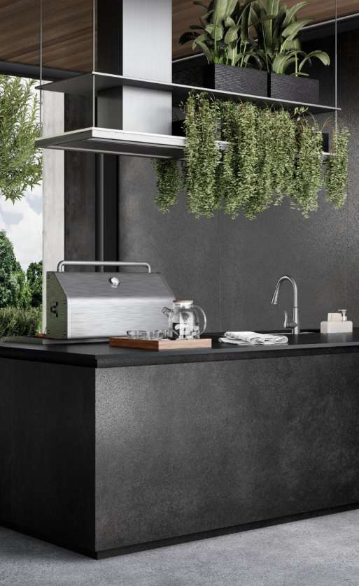 Caesarstone<sup>®</sup> Graphite Metal™ 311 porcelain outdoor kitchen island benchtop with hanging greenery and stainless steel appliances