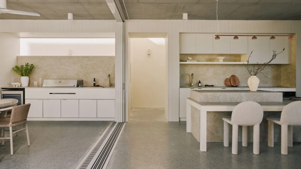 Contemporary kitchen featuring Caesarstone<sup>®</sup> porcelain surface island and splashback, paired with deep green cabinetry, timber shelving and warm brass accents