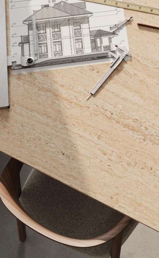 Caesarstone<sup>®</sup> Travina™ 551 porcelain surface detail showing layered beige banding and ochre flecks on architectural drafting table with chair