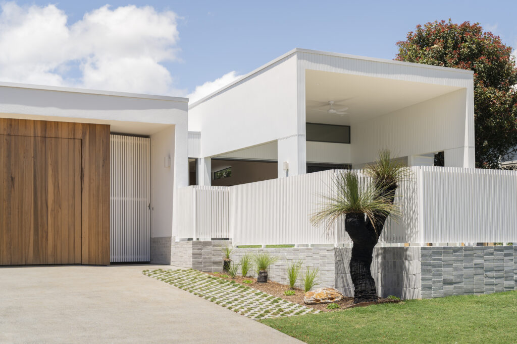 Contemporary Buderim home exterior with white facade, timber garage door and landscaped frontage