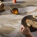 Caesarstone Antikella™ 536 porcelain benchtop with gold veining, styled with sourdough bread and butter in a contemporary kitchen setting