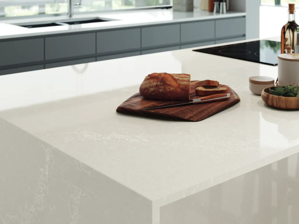 White marble-look Caesarstone<sup>®</sup> benchtop with soft veining on a kitchen island in a contemporary home, styled with a timber board and fresh bread.