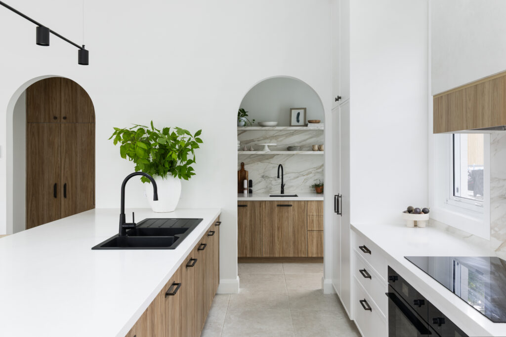 Kitchen view towards arched butler’s pantry with Mirabel™ porcelain surfaces, black tapware and warm timber joinery