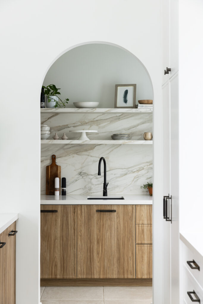 Arched entry to butler’s pantry showing Mirabel™ porcelain splashback, styled open shelving and timber joinery beyond