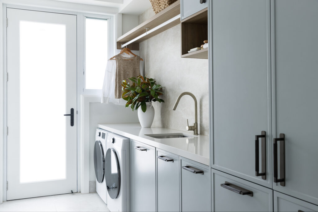 Laundry with Organic White™ benchtop, muted blue cabinetry, brushed nickel tapware and timber shelving in Seaforth home