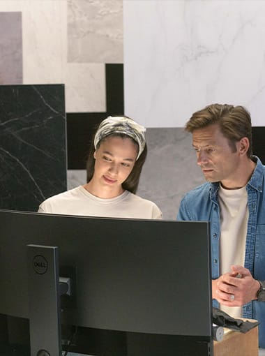 Designers reviewing plans at a monitor, with dark veined large-format surfaces displayed on the wall behind them.