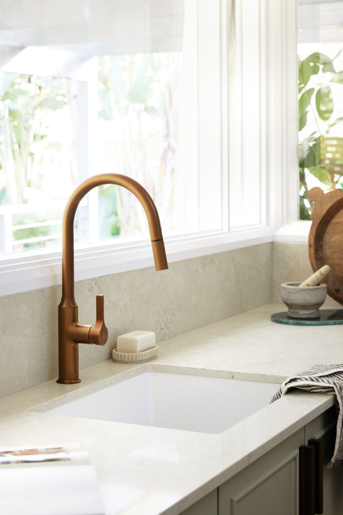 Close-up of copper tapware against a Caesarstone<sup>®</sup> Sedara benchtop and sage green cabinetry.