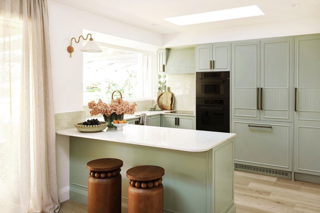 Renovated coastal kitchen with sage green cabinetry, an integrated fridge, black ovens and a Caesarstone<sup>®</sup> Sedara island benchtop.