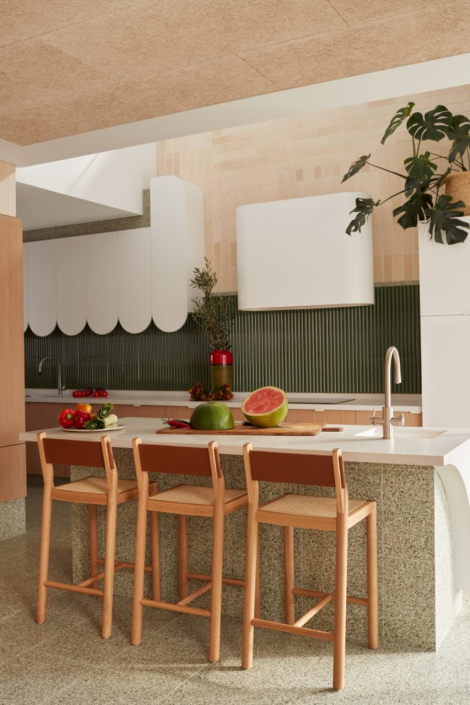 Architectural kitchen featuring a green fluted tiled splashback, terracotta details, timber stools, and a Caesarstone<sup>®</sup> Fresh Concrete island benchtop by Neil Cownie.