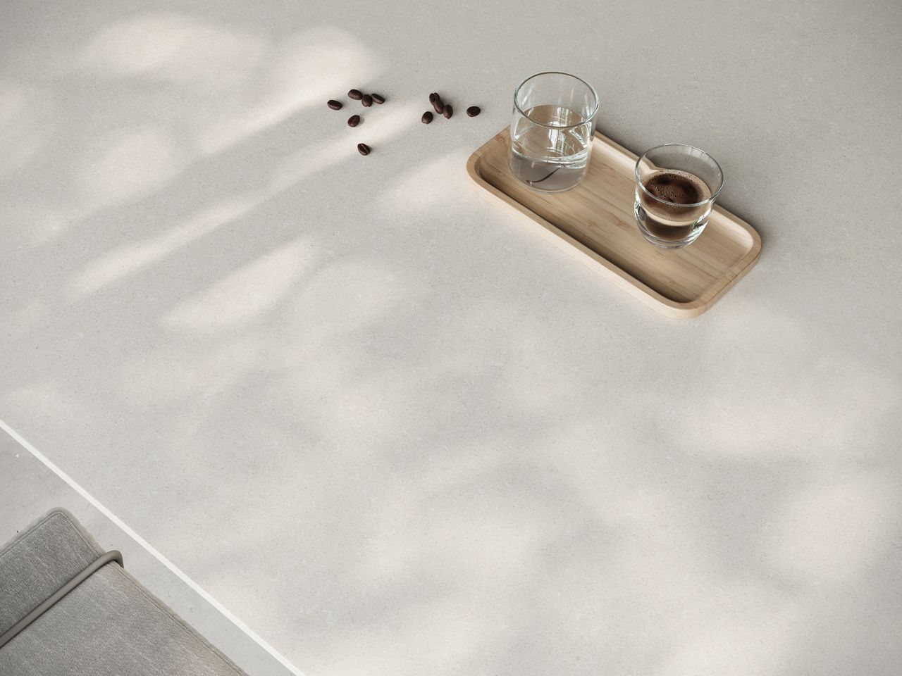 Close-up of Caesarstone<sup>®</sup> Organic White benchtop texture, styled with a timber tray, coffee and water glasses.