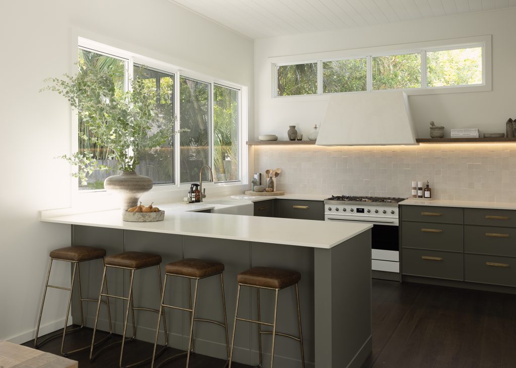 Dark olive green kitchen cabinets with Caesarstone<sup>®</sup> Cloudburst Concrete benchtop and warm brass pulls by Studio Haus Co.