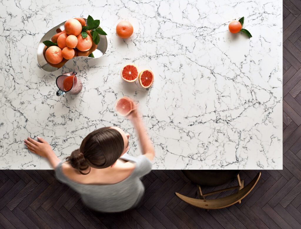 Overhead view of a person at a white Caesarstone<sup>®</sup> White Attica kitchen island benchtop with dark veining.