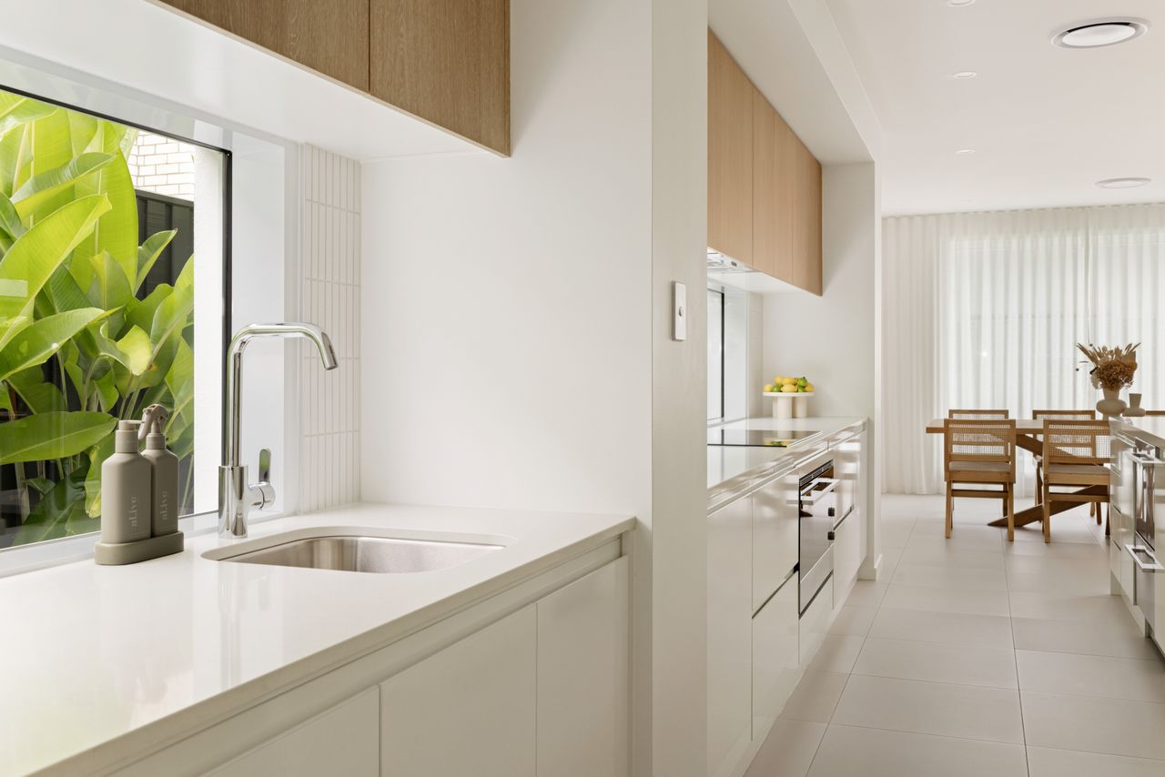 Galley kitchen with a Caesarstone<sup>®</sup> Organic White benchtop and sink beneath a window overlooking greenery.
