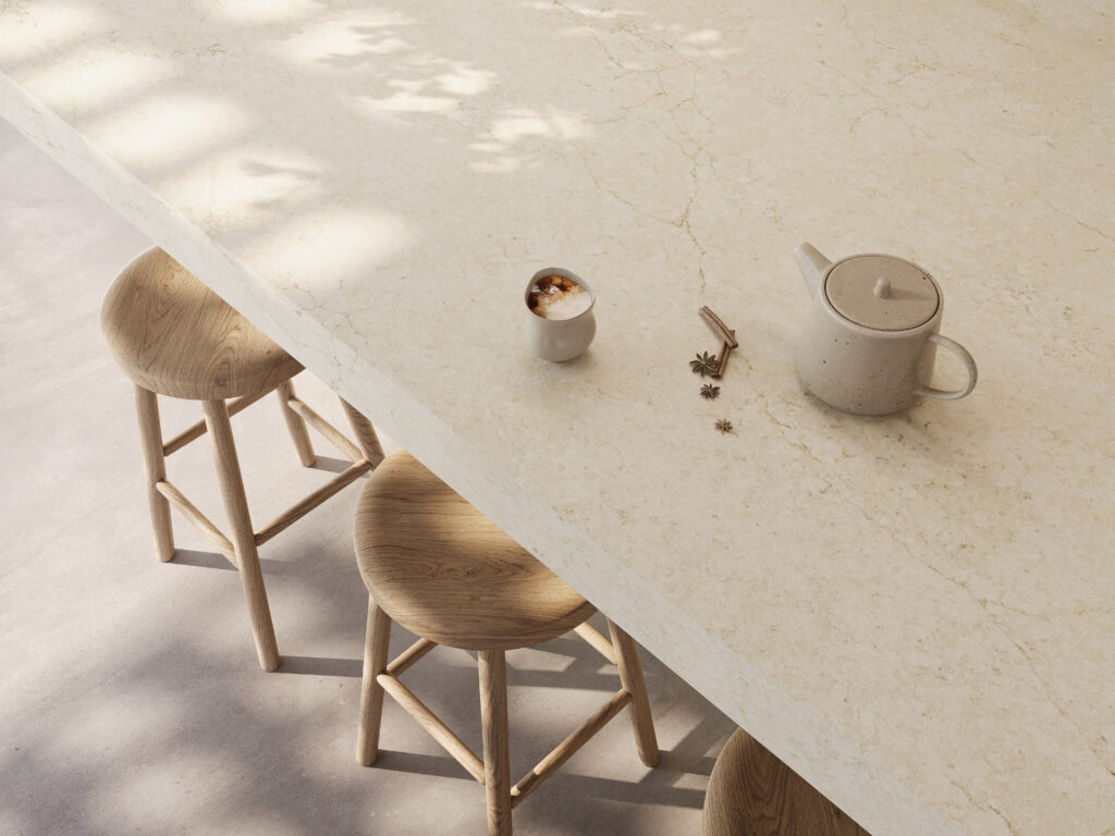 Morning coffee and teapot sitting on a cream Caesarstone<sup>®</sup> Sedara kitchen benchtop with light timber stools tucked underneath.