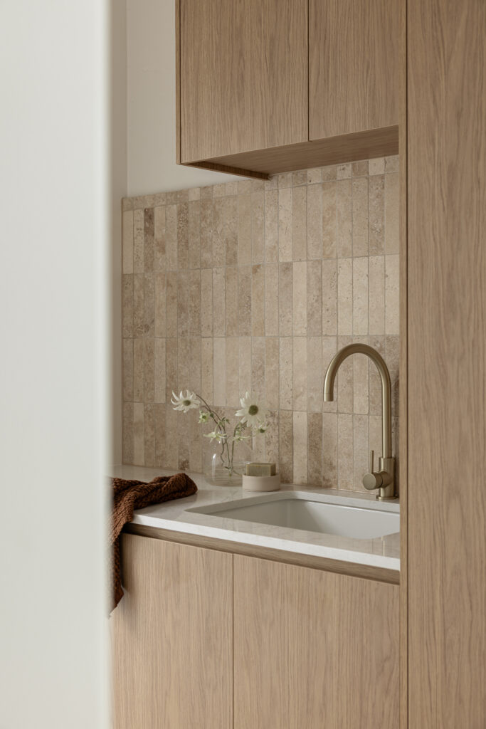 Laundry sink in Caesarstone Lunar Frost with travertine-look splashback tile and oak cabinetry.