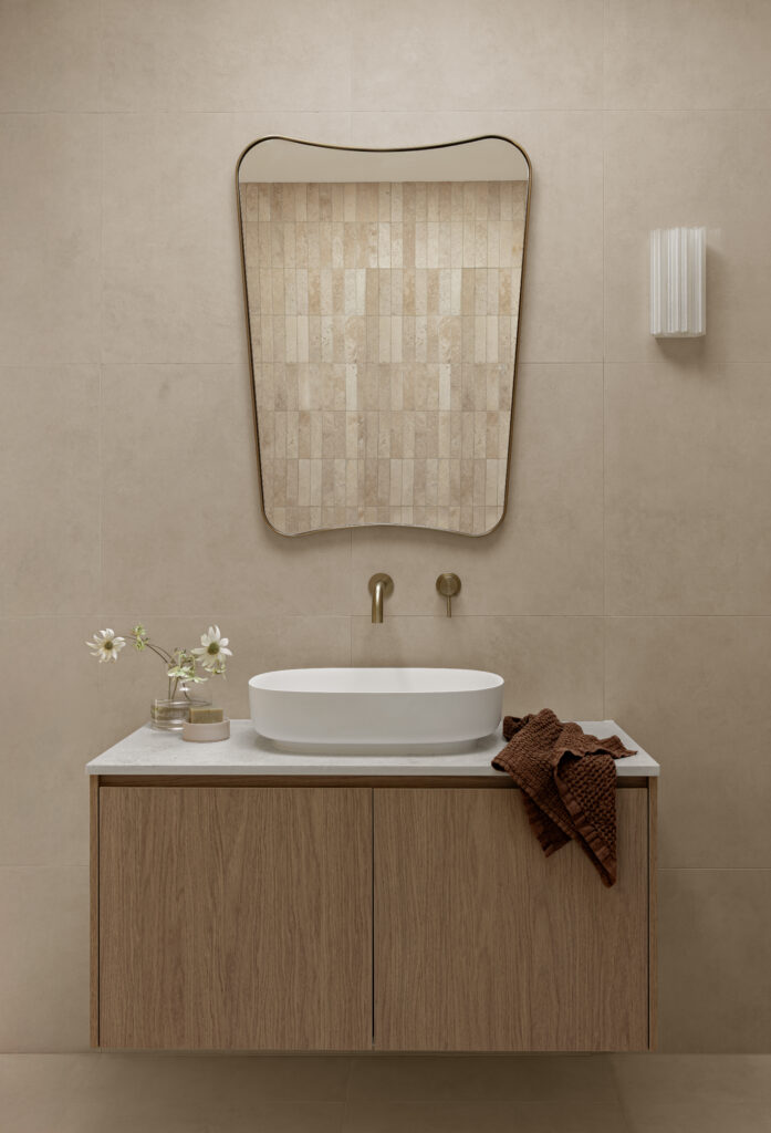Warm neutral bathroom with timber vanity, white Caesarstone benchtop, oval basin and sculptural mirror.