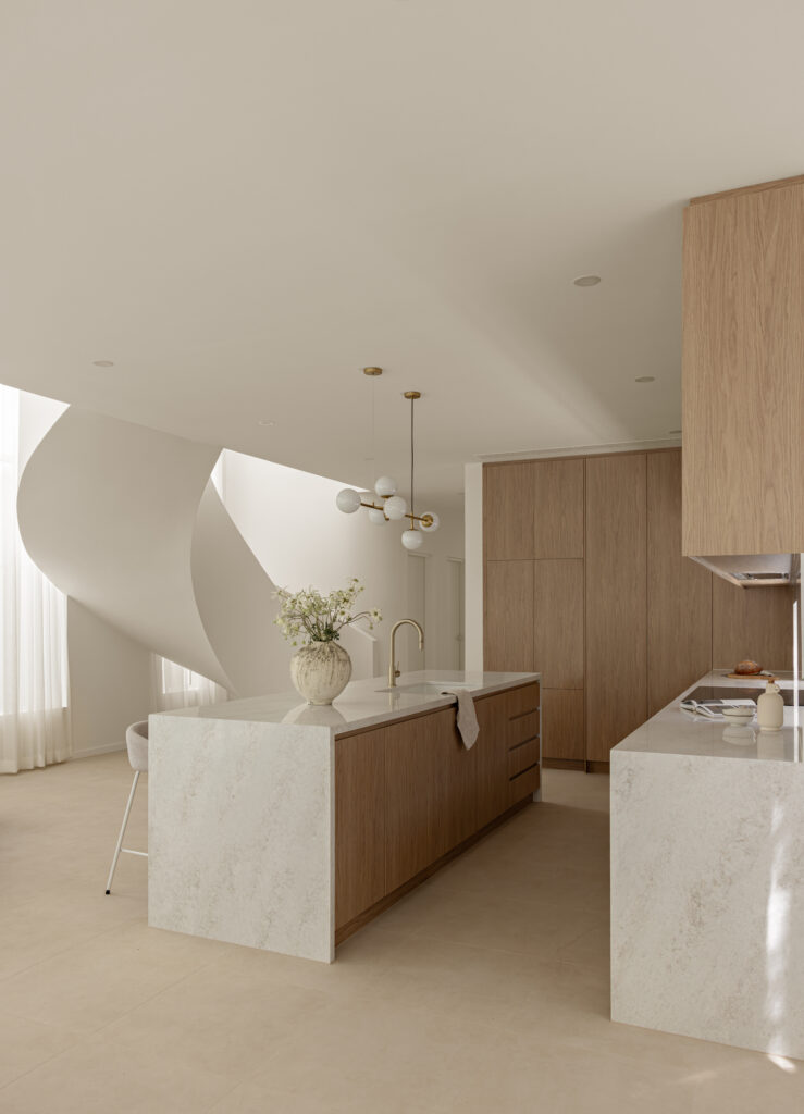 Kitchen island and servery in Caesarstone Lunar Frost with waterfall edges, oak cabinetry and sculptural staircase.