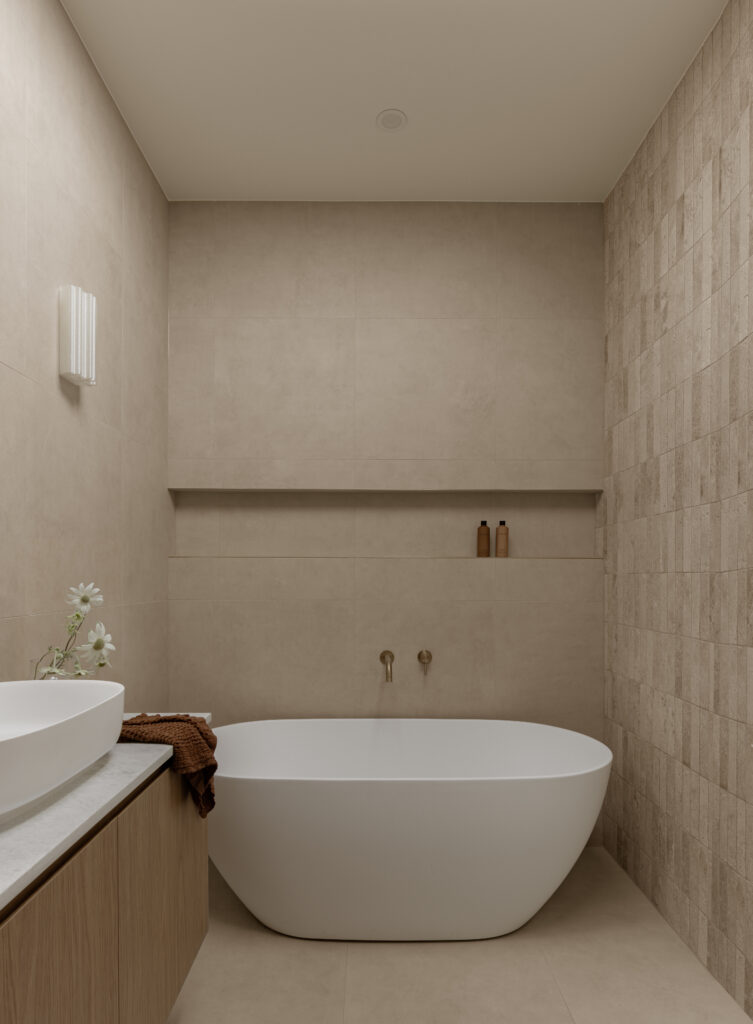 Freestanding oval bathtub against tiled wall with wall-mounted brass tapware.