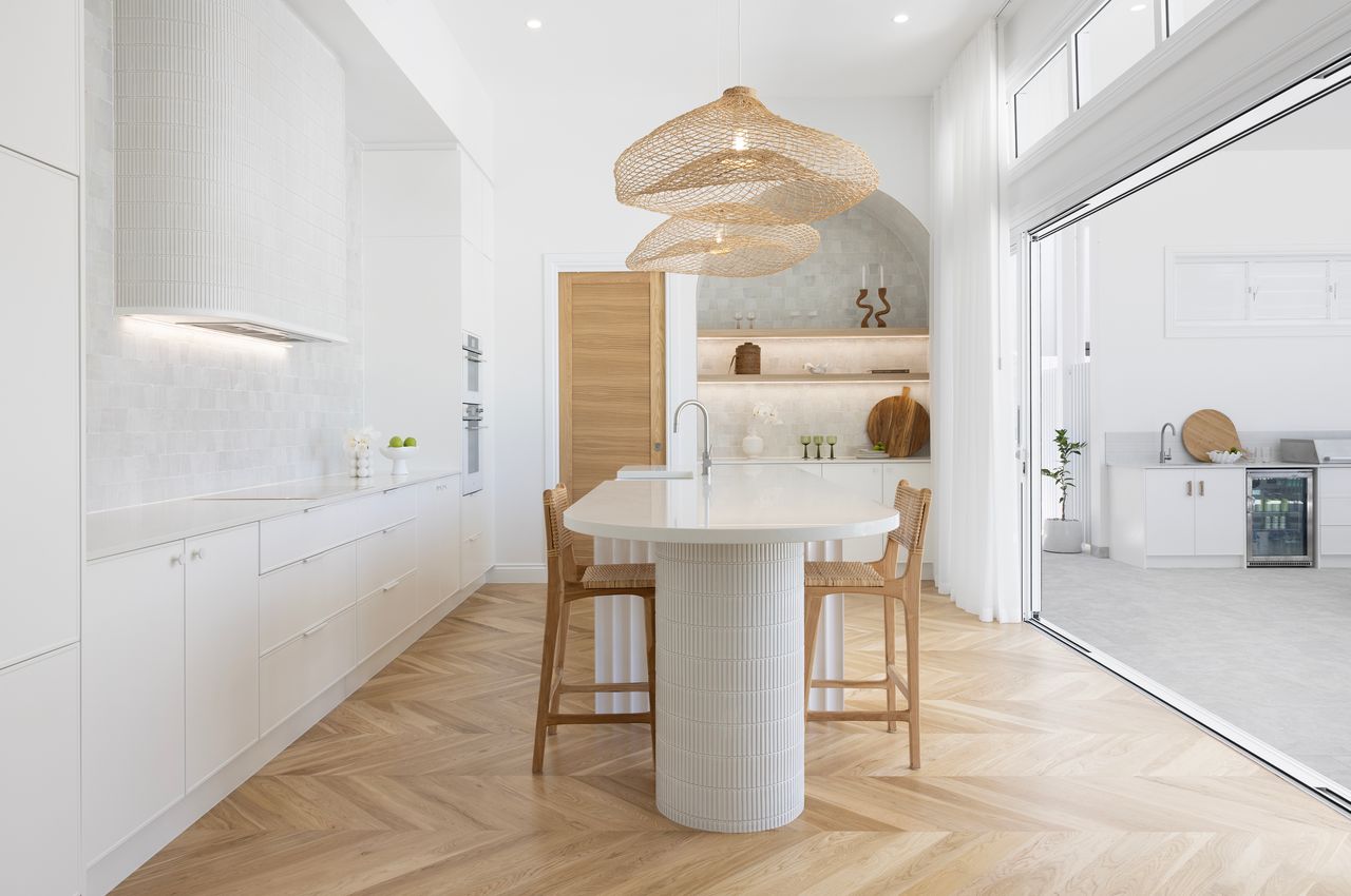 Caesarstone<sup>®</sup> Organic White kitchen island and benchtops in an open dining space with herringbone timber flooring.