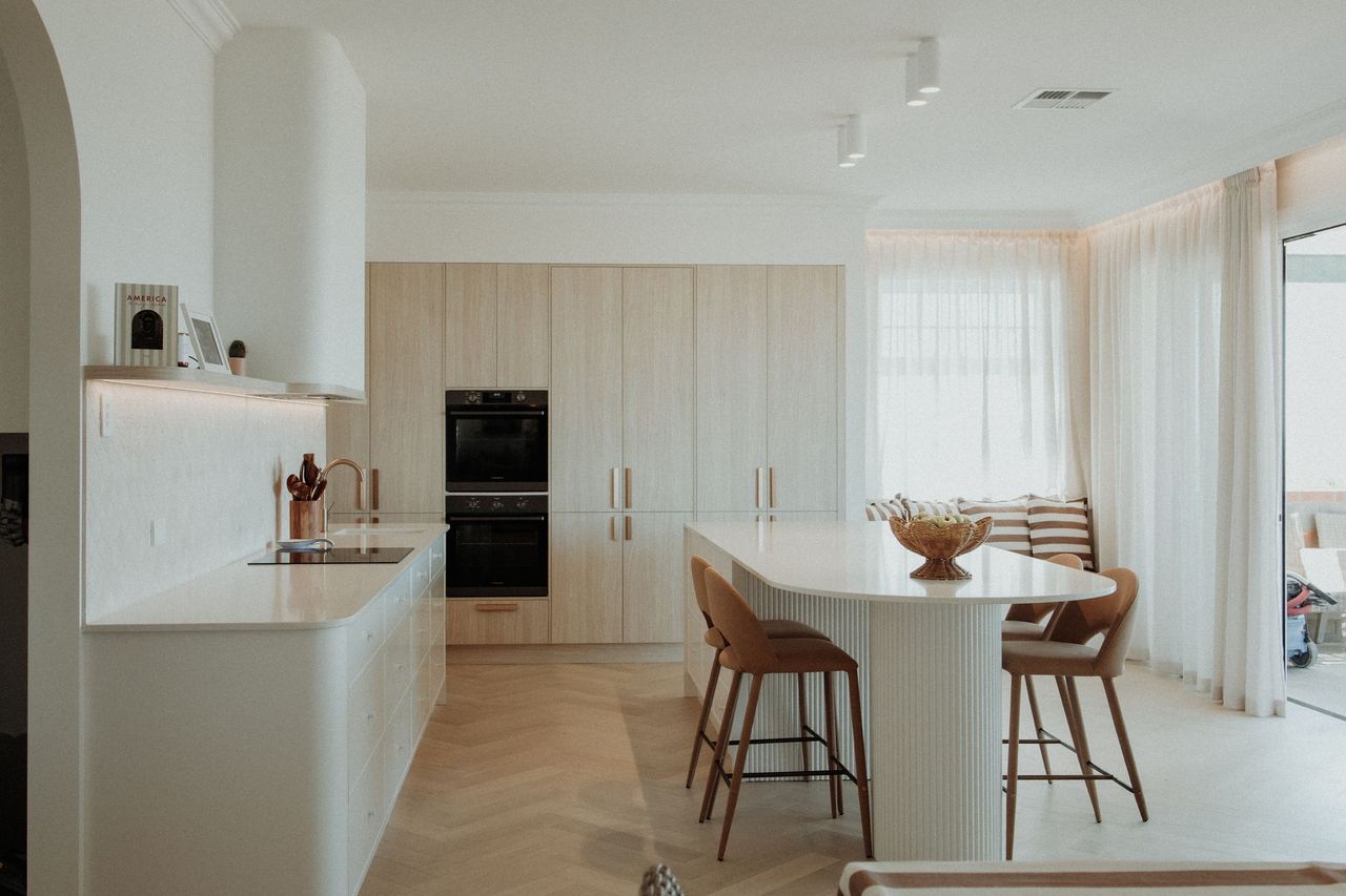 Kitchen benchtops and island in Caesarstone<sup>®</sup> Organic White, with curved cabinetry and a round dining table.