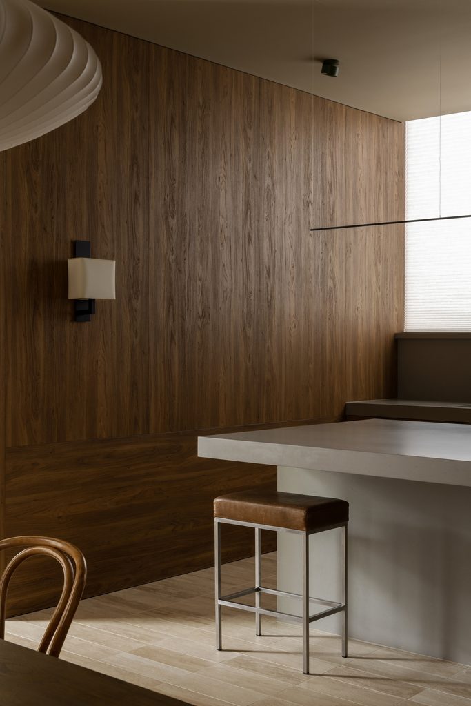 Timber panelling wrapping a corner of the kitchen, with a leather stool set at a Caesarstone<sup>®</sup> Raw Concrete bench, lit by a narrow window.